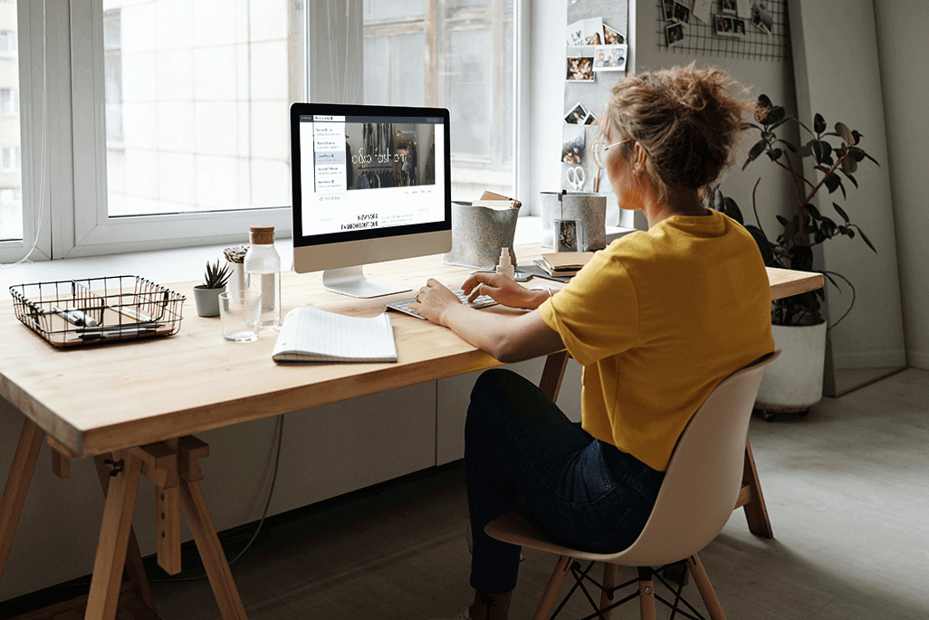 Junge Frau im gelben T-Shirt am Schreibtisch vor dem Imac sitzend.